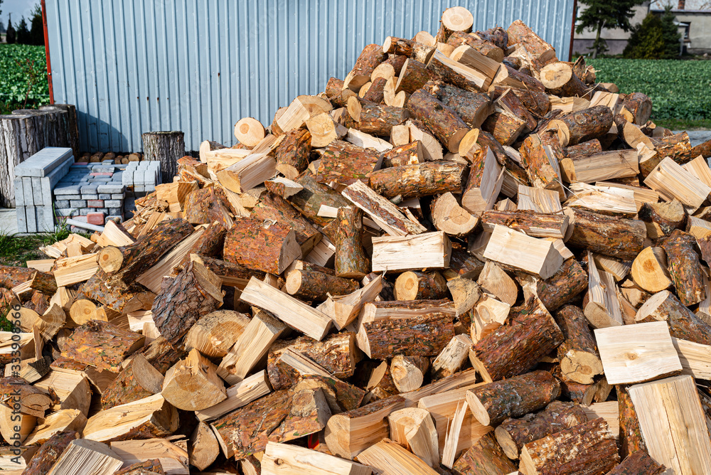 A firewood stacked in a pile, lying on the property near the metal garage, wooden background. A firewood stacked in a pile, lying on the property near the metal garage, wooden background.