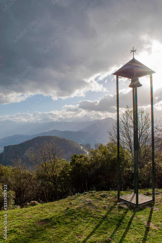 Christian bell and cross next to the small Orthodox church with mountain view. Meteora, Greece