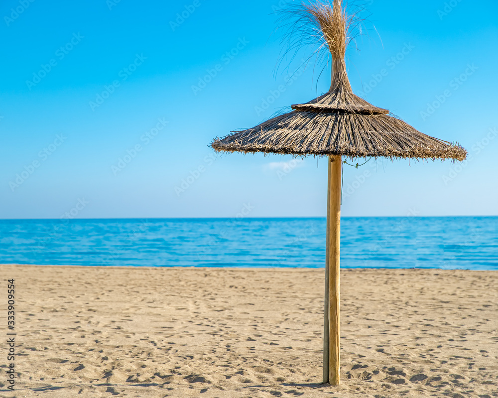 Straw umbrella on sea beach, blue sky