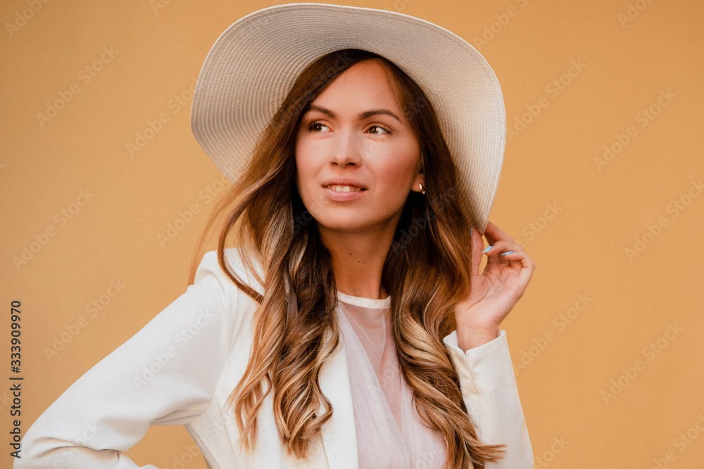 Outdoor close up fashion portrait of young beautiful happy smiling lady wearing white dress, stylish straw wide brim hat, posing on yellow wall. City Outdoor close up fashion portrait of young beautiful happy smiling lady wearing white dress, stylish straw wide brim hat, posing on yellow wall. City