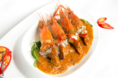 Fired giant freshwater prawns fired in spicy coconut sauce serving on white plate top with coconut cream decorate with paprika