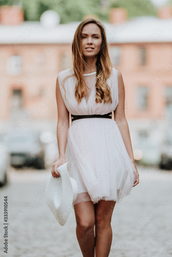 Outdoor fashion portrait of young beautiful happy smiling lady wearing white dress, stylish straw wide brim hat, posing on street. City Outdoor fashion portrait of young beautiful happy smiling lady wearing white dress, stylish straw wide brim hat, posing on street. City