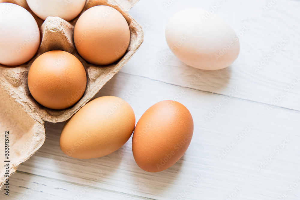 Brown and white organic chicken eggs in a brown paper box placed on a white wooden table. Eggs provide protein, suitable for health lovers. Brown and white organic chicken eggs in a brown paper box placed on a white wooden table. Eggs provide protein, suitable for health lovers.