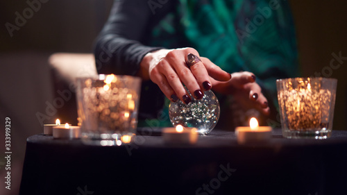 Close-up of fortuneteller female divining on magic ball at table with burning candles