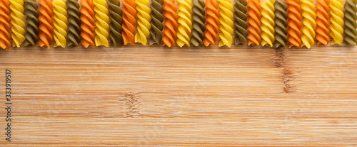 Raw multicolored tricolore fusilli pasta scattered on brown wooden background. Horizontal frame. Top side decoration.