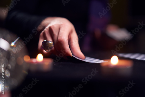 Close-up of woman fortuneteller's hands with fortune-telling cards at table with candles
