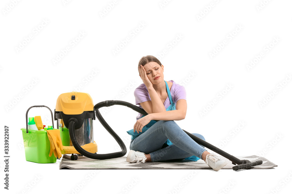 Tired woman with vacuum cleaner sitting on carpet against white background Tired woman with vacuum cleaner sitting on carpet against white background