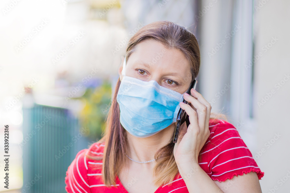 woman with mask is out to home terrace using mobile phone during quarantine due to coronavirus covid19 pandemic.