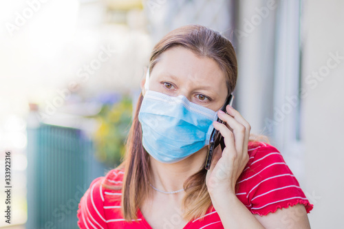 woman with mask is out to home terrace using mobile phone during quarantine due to coronavirus covid19 pandemic.