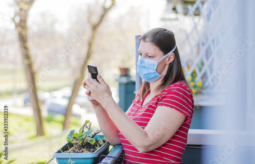 woman with mask is out to home terrace using mobile phone during quarantine due to coronavirus covid19 pandemic. photo