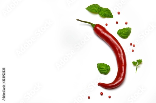 chili pepper pod next to Basil leaves and pepper on a white