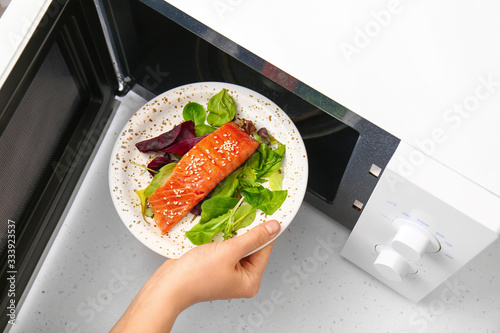 Canvas Print Woman putting plate with food in microwave oven