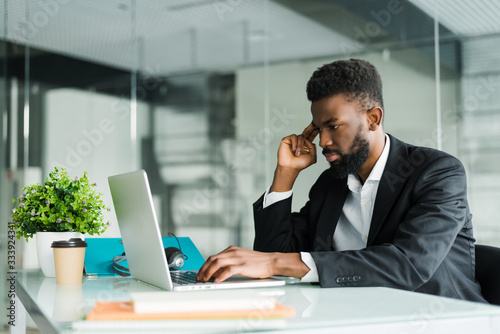 Thoughtful young african american businessman working on laptop in office
