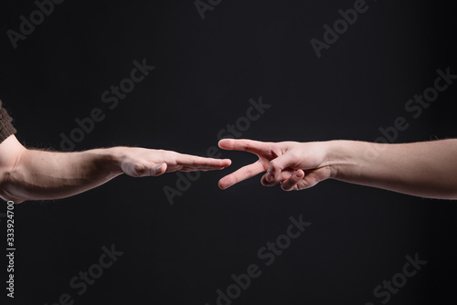 Men's hands on a dark background, show a game of stone, scissors, paper. The concept of confrontation and rivalry, games