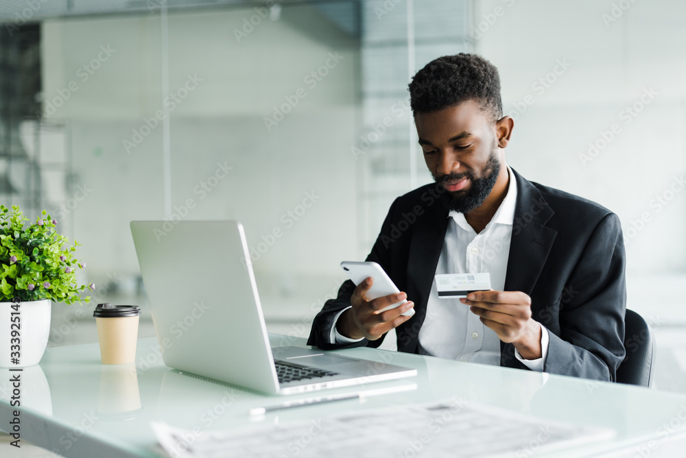 African American man paying with credit card online while making orders via mobile Internet making transaction using mobile bank application. African American man paying with credit card online while making orders via mobile Internet making transaction using mobile bank application.