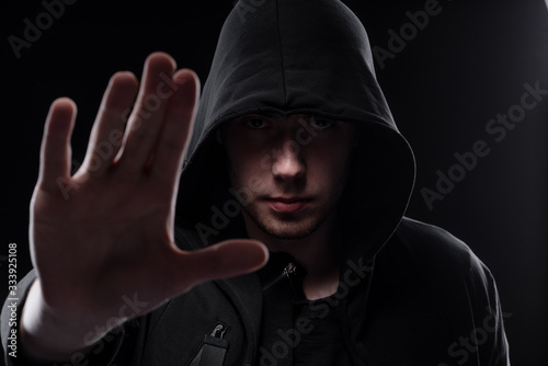 A man in a black hood on a black background, studio photography. The idea of mysticism, mystery, crime and deception
