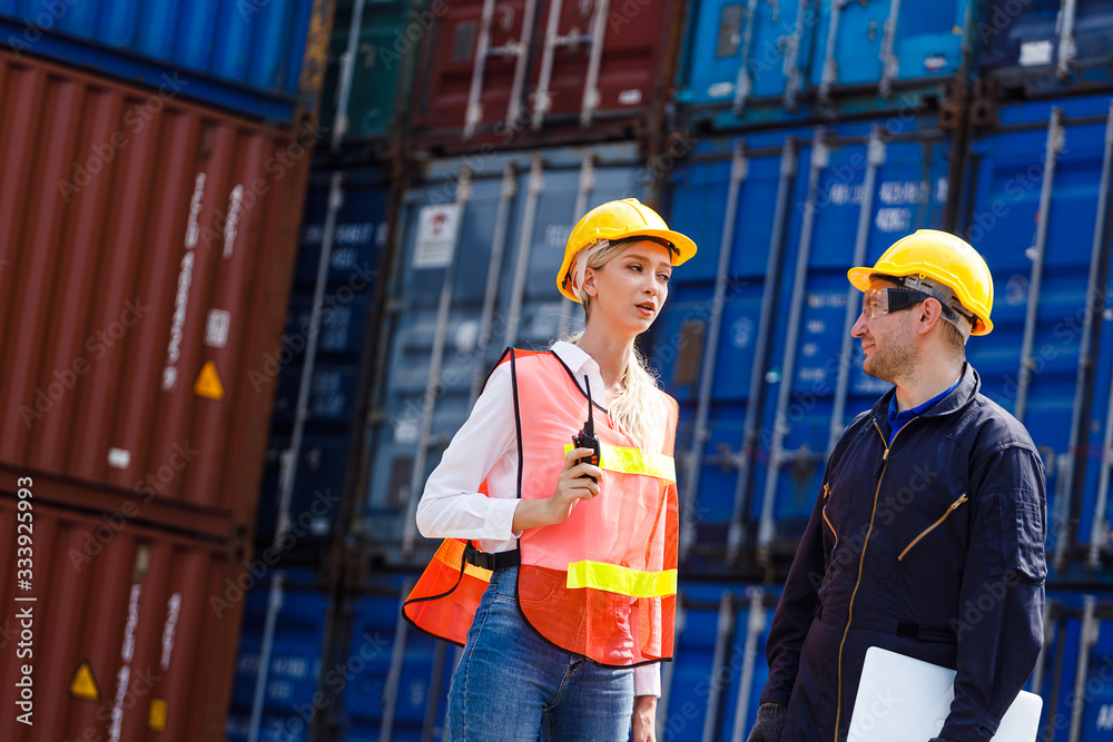 Technician or engineer with yellow helmet use walkie-talkie to contact with co-worker in cargo container shipping yard. Industry of logistics network concept Technician or engineer with yellow helmet use walkie-talkie to contact with co-worker in cargo container shipping yard. Industry of logistics network concept