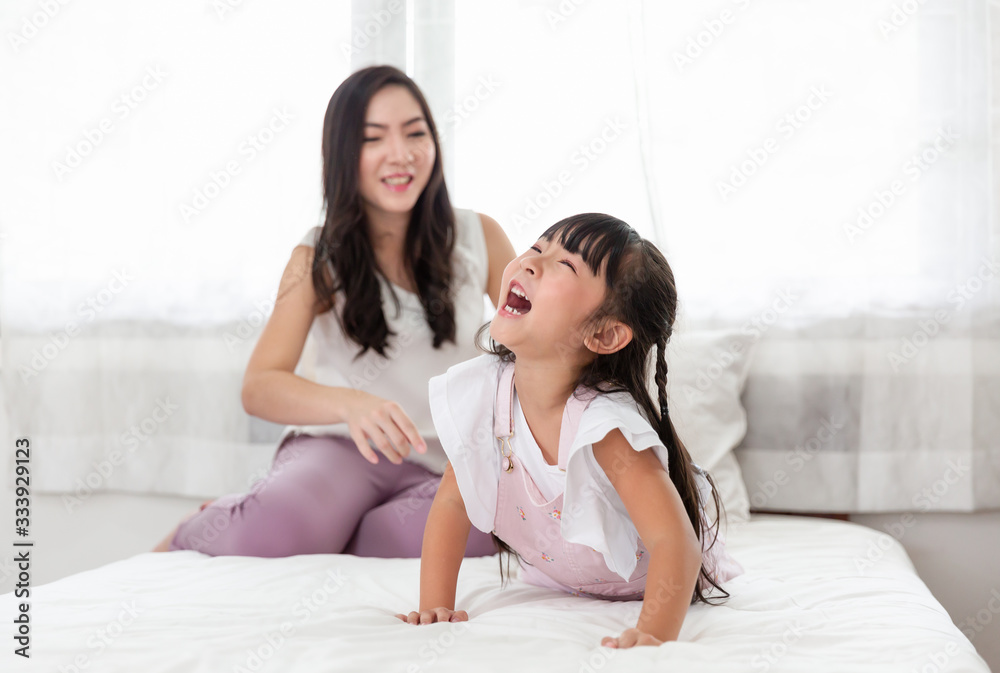 Happy young Asian Mother and daughter enjoy on the bed near windows at home. Mom and little adorable spend time and laughing together at home Happy young Asian Mother and daughter enjoy on the bed near windows at home. Mom and little adorable spend time and laughing together at home