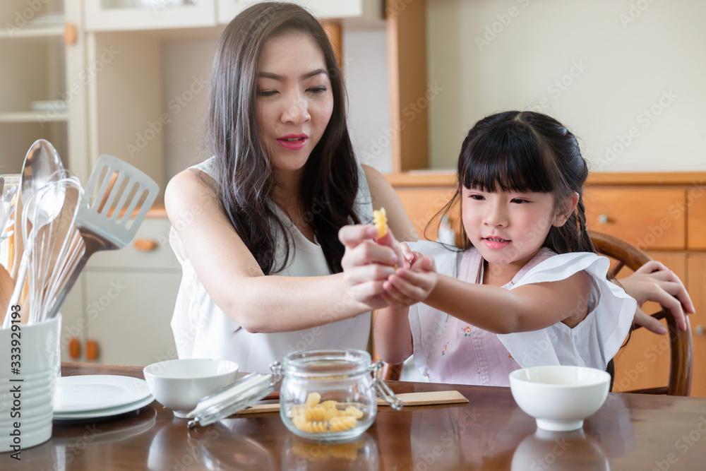 Mom and daughter spend time together at home. Young Asian mother teaches little adorable daughter make breakfast together in the kitchen room at home. Housewife concept. Mom and daughter spend time together at home. Young Asian mother teaches little adorable daughter make breakfast together in the kitchen room at home. Housewife concept.