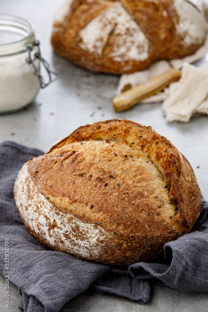 Rustic wheat bread with flax on a napkin. Sourdough artisan bread and jar of flour