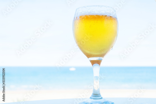 Glass of beer on the table against the beach. Beer with foam on the background of the sea.