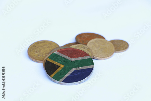 South Africa flag on the coin with heap of South African Rand money on the white background. Concept of finance.