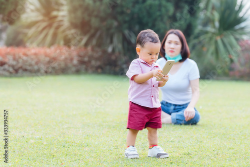 Mother and son in garden. Asian woman sitting on lawn and her son standing with telephone in hand.