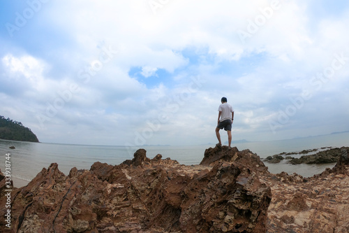 Man standing on top of the rock and looking at the beach.
