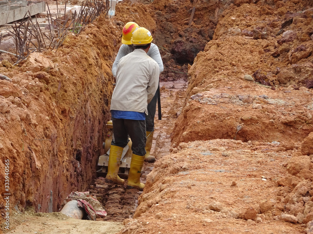 SEREMBAN, MALAYSIA -MARCH 03, 2020: Construction workers are using the baby compactor to level and compact the soil at the construction site. SEREMBAN, MALAYSIA -MARCH 03, 2020: Construction workers are using the baby compactor to level and compact the soil at the construction site.