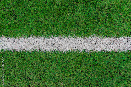 White stripe on the green soccer field top view. White line on artificial football field