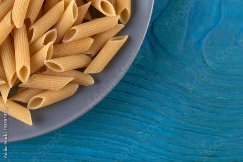 A lot of raw pasta penne on a patr of plate at blue wooden background horizontal photo