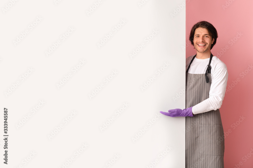 Cleaning Promo. Smiling male janitor pointing at copy space on white advertisement board Cleaning Promo. Smiling male janitor pointing at copy space on white advertisement board