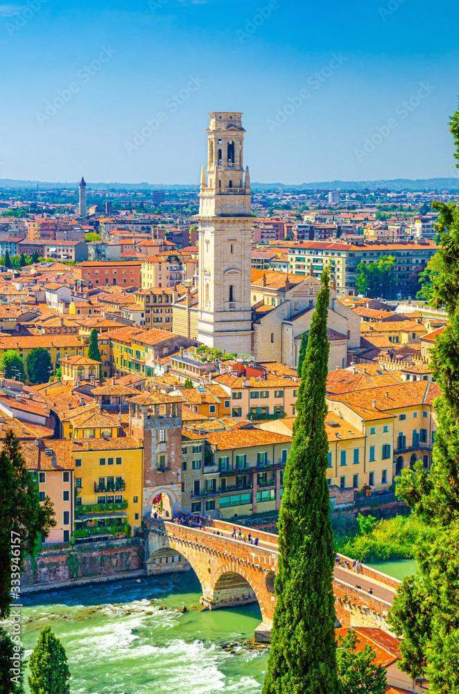 Fototapeta premium Vertical view of Verona historical city centre, Ponte Pietra bridge across Adige river, tower of Verona Cathedral, Duomo di Verona, red tiled roofs buildings, Veneto Region, Italy. Verona cityscape