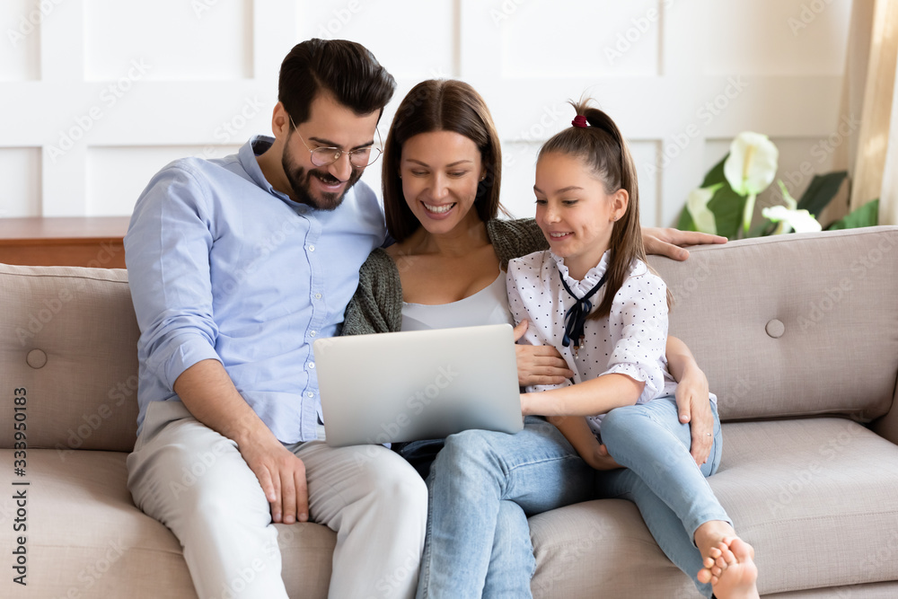 Happy bearded man embracing smiling wife and adorable school aged girl, watching funny video on computer. Affectionate family of three playing game on laptop or shopping online in internet store. Happy bearded man embracing smiling wife and adorable school aged girl, watching funny video on computer. Affectionate family of three playing game on laptop or shopping online in internet store.