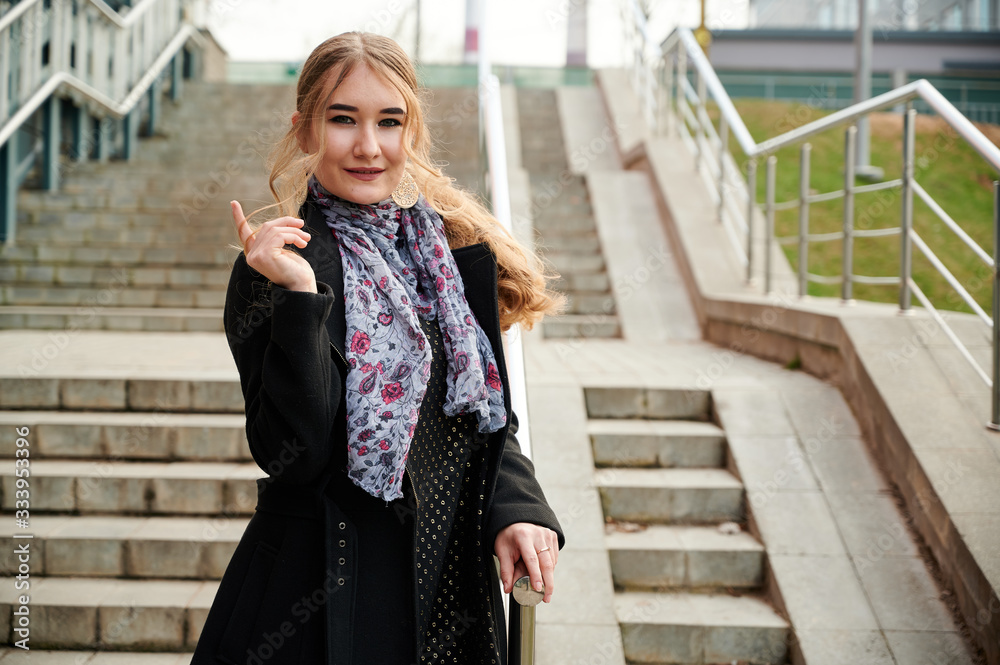 Photo of a fashionable blonde girl in a coat on the stairs outdoors in the spring city