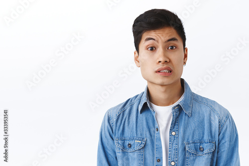 Portrait of concerned, unsure young asian man feeling awkward or doubtful, have something to say, look indecisive, faing troublesome situation, being bothered, white background photo