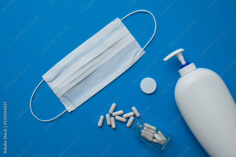 facial disposable medical mask, white pills and liquid hand soap isolated on blue background. facial disposable medical mask, white pills and liquid hand soap isolated on blue background.