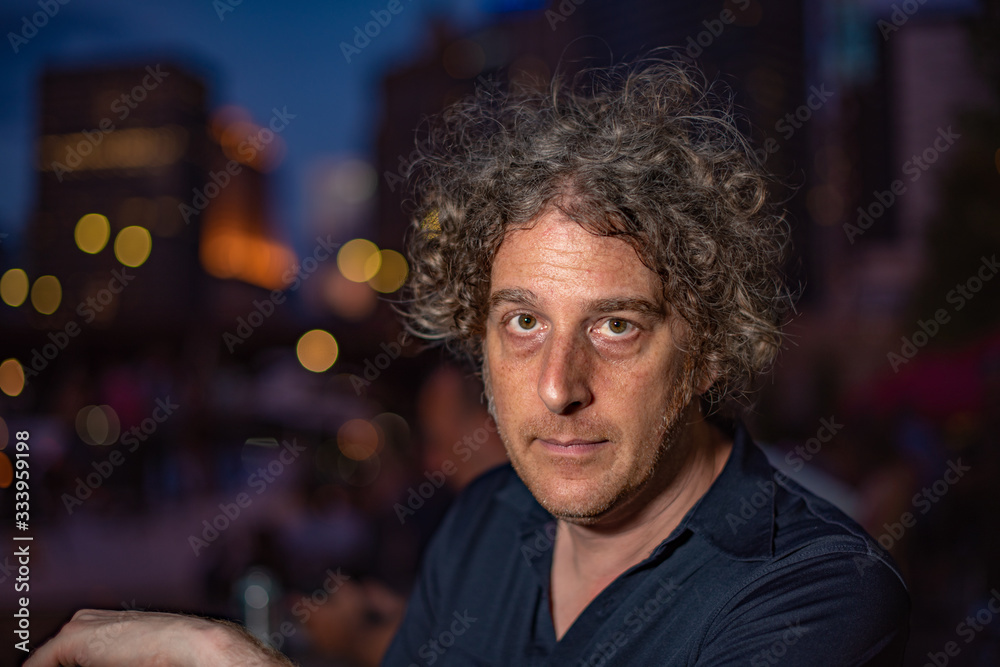 A middle aged man enjoys an evening out in the city, with bright lights behind him.