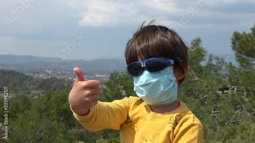 Fethiye, Turkey - 27d of March 2020: 4K Boy in protective mask learns to show thumbs-up, countryside in the background, crystal child photo