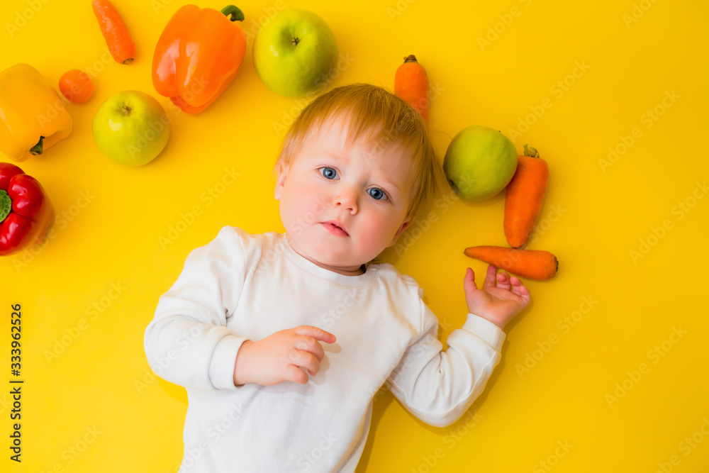 Healthy child nutrition, food background, top view. Smiling baby 8 months old surrounded with different fresh fruits and vegetables on yellow background. Baby first solid feeding.baby with vegetables Healthy child nutrition, food background, top view. Smiling baby 8 months old surrounded with different fresh fruits and vegetables on yellow background. Baby first solid feeding.baby with vegetables