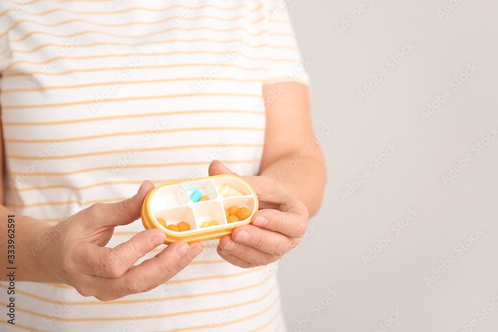 Mature woman with pills box on light background, closeup Mature woman with pills box on light background, closeup