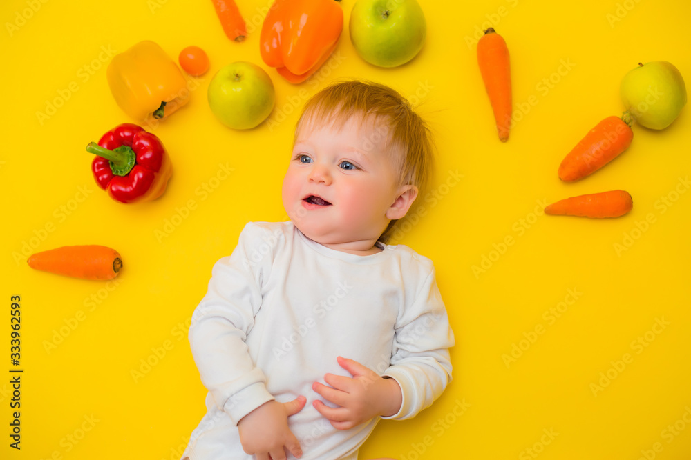 Healthy child nutrition, food background, top view. Smiling baby 8 months old surrounded with different fresh fruits and vegetables on yellow background. Baby first solid feeding.baby with vegetables Healthy child nutrition, food background, top view. Smiling baby 8 months old surrounded with different fresh fruits and vegetables on yellow background. Baby first solid feeding.baby with vegetables
