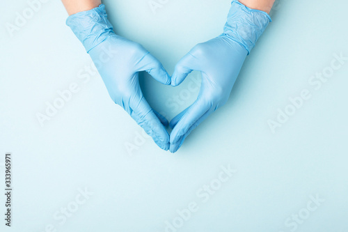 Doctor's hands in medical gloves in shape of heart on blue background with copy space. photo