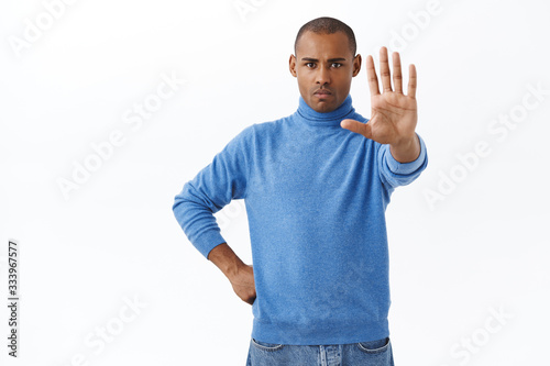 Portrait of confident, serious-looking young man warning as security, stretch hand forward in stop, prohibition gesture, frowning determined, want to quit people coming outside during quarantine