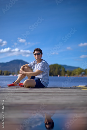 Handsome man relax in sunglasses and sitting on the pier and looking to camera.Summer vacations