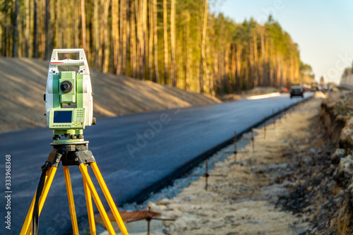 Surveyors equipment (theodolite or total positioning station) on the construction site of the road or building with construction machinery background