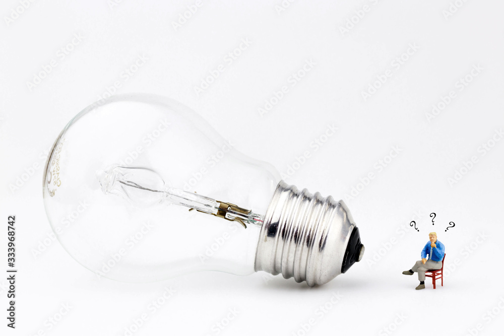 miniature man sitting on a chair next to a lihgt bulb with question marks over his head miniature man sitting on a chair next to a lihgt bulb with question marks over his head
