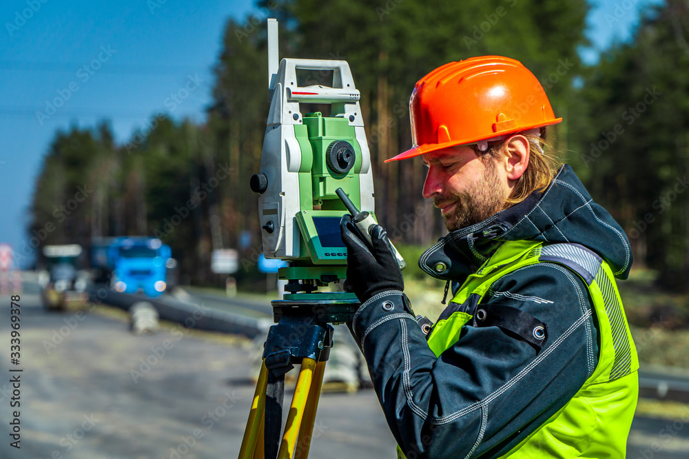 Surveyor engineer with equipment (theodolite or total positioning station) on the construction site of the road or building with construction machinery background Surveyor engineer with equipment (theodolite or total positioning station) on the construction site of the road or building with construction machinery background