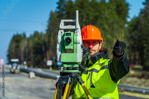 Surveyor engineer with equipment (theodolite or total positioning station) on the construction site of the road or building with construction machinery background