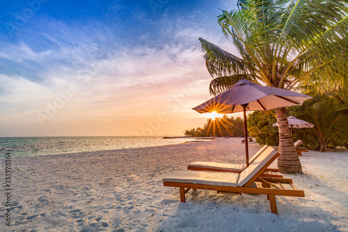 Fototapeta Naklejka Na Ścianę i Meble -  Beautiful tropical sunset scenery, two sun beds, loungers, umbrella under palm tree. White sand, sea view with horizon, colorful twilight sky, calmness and relaxation. Inspirational beach resort hotel